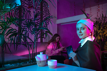 Image showing Beautiful girl with a pearl earring taking lunch in modern cafe, restaurant in neon light