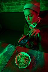 Image showing Beautiful girl with a pearl earring taking lunch in modern cafe, restaurant in neon light