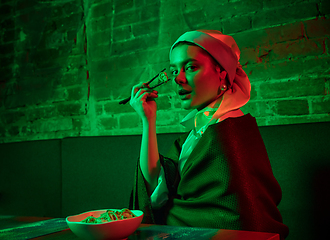 Image showing Beautiful girl with a pearl earring taking lunch in modern cafe, restaurant in neon light