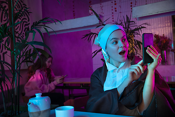 Image showing Beautiful girl with a pearl earring taking lunch in modern cafe, restaurant in neon light