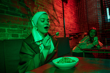 Image showing Beautiful girl with a pearl earring taking lunch in modern cafe, restaurant in neon light