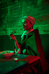 Image showing Beautiful girl with a pearl earring taking lunch in modern cafe, restaurant in neon light