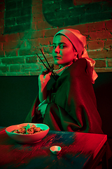 Image showing Beautiful girl with a pearl earring taking lunch in modern cafe, restaurant in neon light