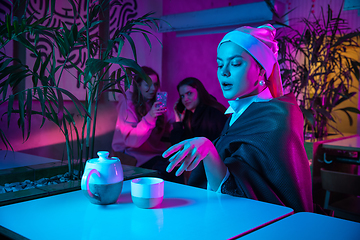 Image showing Beautiful girl with a pearl earring taking lunch in modern cafe, restaurant in neon light