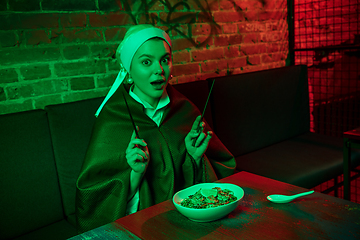 Image showing Beautiful girl with a pearl earring taking lunch in modern cafe, restaurant in neon light