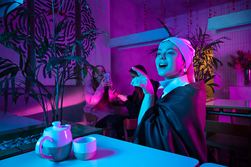 Image showing Beautiful girl with a pearl earring taking lunch in modern cafe, restaurant in neon light