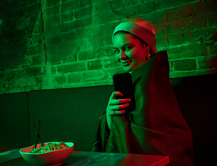 Image showing Beautiful girl with a pearl earring taking lunch in modern cafe, restaurant in neon light