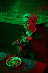 Image showing Beautiful girl with a pearl earring taking lunch in modern cafe, restaurant in neon light