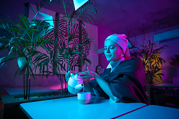 Image showing Beautiful girl with a pearl earring taking lunch in modern cafe, restaurant in neon light