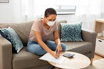 Image showing woman in mask with papers and calculator at home