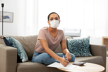 Image showing woman in mask with papers and calculator at home