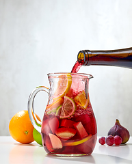 Image showing red wine pouring into jug of cutted fruits