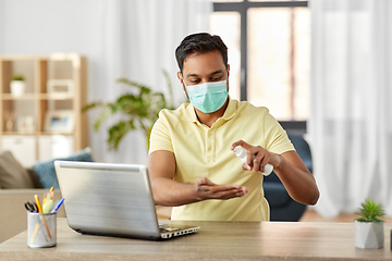 Image showing man in mask using hand sanitizer at home office