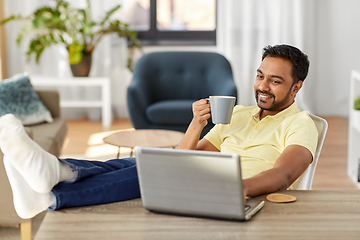 Image showing man with laptop drinking coffee at home office