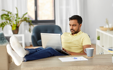 Image showing man with laptop resting feet on table at home