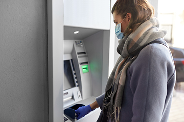 Image showing woman in mask and glove entreing code at atm