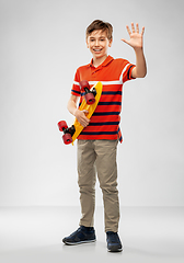 Image showing smiling boy with short skateboard waving hand