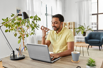 Image showing man with laptop recording voice on phone at home