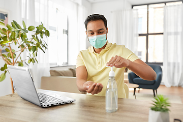Image showing man in mask using hand sanitizer at home office