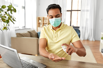 Image showing man in mask using hand sanitizer at home office