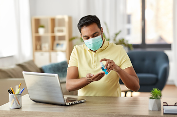 Image showing man in mask using hand sanitizer at home office