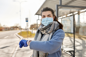 Image showing woman in mask looking at wristwatch at bus stop