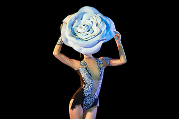 Image showing Young female dancer with huge floral hat in neon light on black background