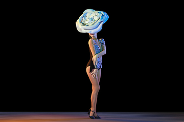 Image showing Young female dancer with huge floral hat in neon light on black background