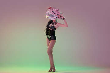 Image showing Young female dancer with huge floral hats in neon light on gradient background