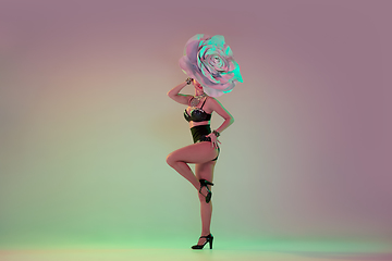 Image showing Young female dancer with huge floral hats in neon light on gradient background