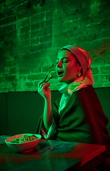 Image showing Beautiful girl with a pearl earring taking lunch in modern cafe, restaurant in neon light