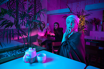 Image showing Beautiful girl with a pearl earring taking lunch in modern cafe, restaurant in neon light