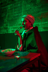 Image showing Beautiful girl with a pearl earring taking lunch in modern cafe, restaurant in neon light