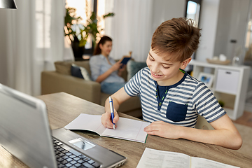 Image showing student boy with book writing to notebook at home