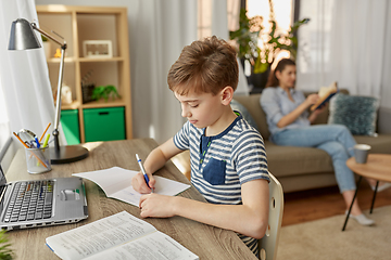 Image showing student boy with book writing to notebook at home