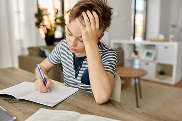 Image showing student boy with book writing to notebook at home