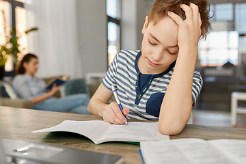 Image showing student boy with book writing to notebook at home