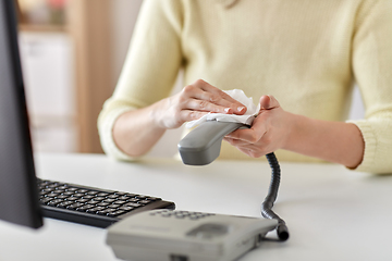 Image showing close up of woman cleaning desk phone with tissue