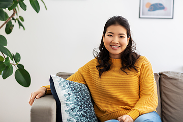 Image showing smiling asian young woman sitting on sofa at home