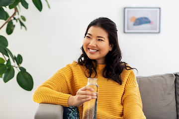 Image showing smiling asian young woman drinking water at home