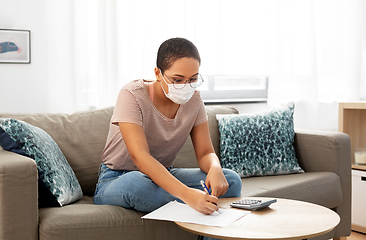 Image showing woman in mask with papers and calculator at home