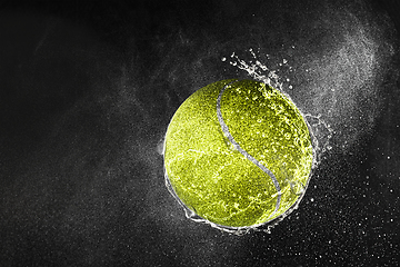 Image showing Tennis ball flying in water drops and splashes isolated on black background