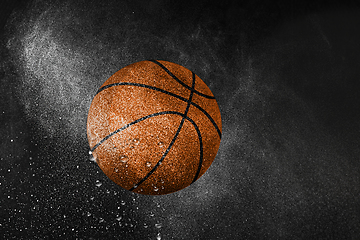 Image showing Basketball ball flying in water drops and splashes isolated on black background