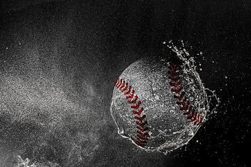 Image showing Baseball ball flying in water drops and splashes isolated on black background