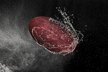 Image showing American football ball flying in water drops and splashes isolated on black background