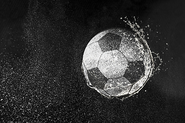 Image showing Football, soccer ball flying in water drops and splashes isolated on black background