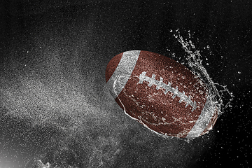 Image showing American football ball flying in water drops and splashes isolated on black background