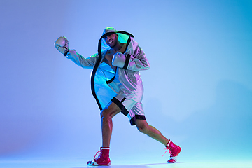 Image showing High-fashion styled man in white outfit pacticing box isolted over gradient background in neon light