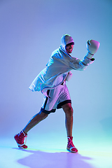 Image showing High-fashion styled man in white outfit pacticing box isolted over gradient background in neon light