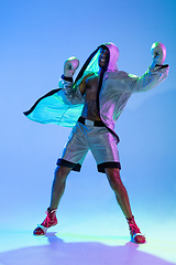 Image showing High-fashion styled man in white outfit pacticing box isolted over gradient background in neon light